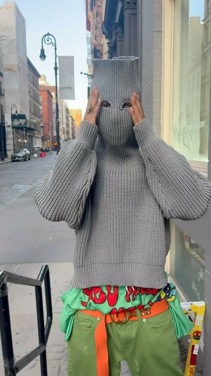 NYC local in eclectic fashion: green pants, colorful shirt, gray knit mask, on a city street experimenting with style.