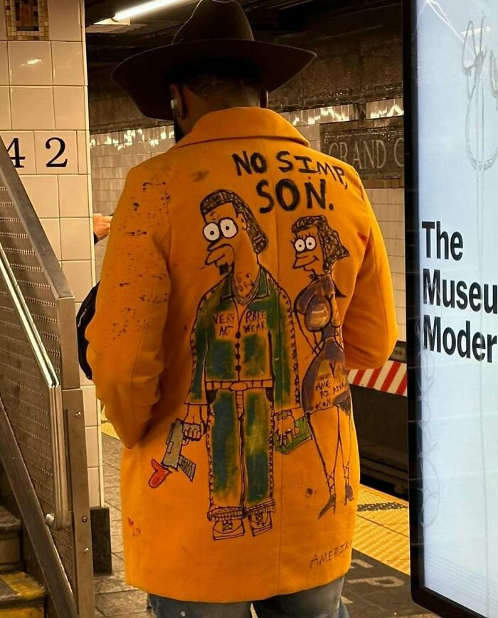 NYC local in subway wearing a vibrant yellow coat with cartoon art, showcasing unique fashion experimentation.