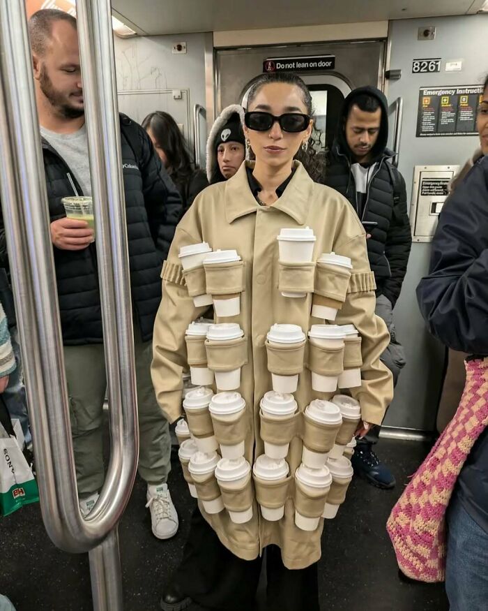 New York local wearing a trench coat covered in coffee cups, showcasing experimental fashion on the subway.