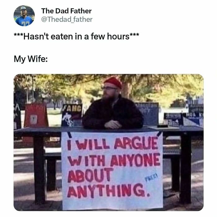 Man sitting at a table with a humorous sign about arguing, capturing the daily joys and struggles of a dad.