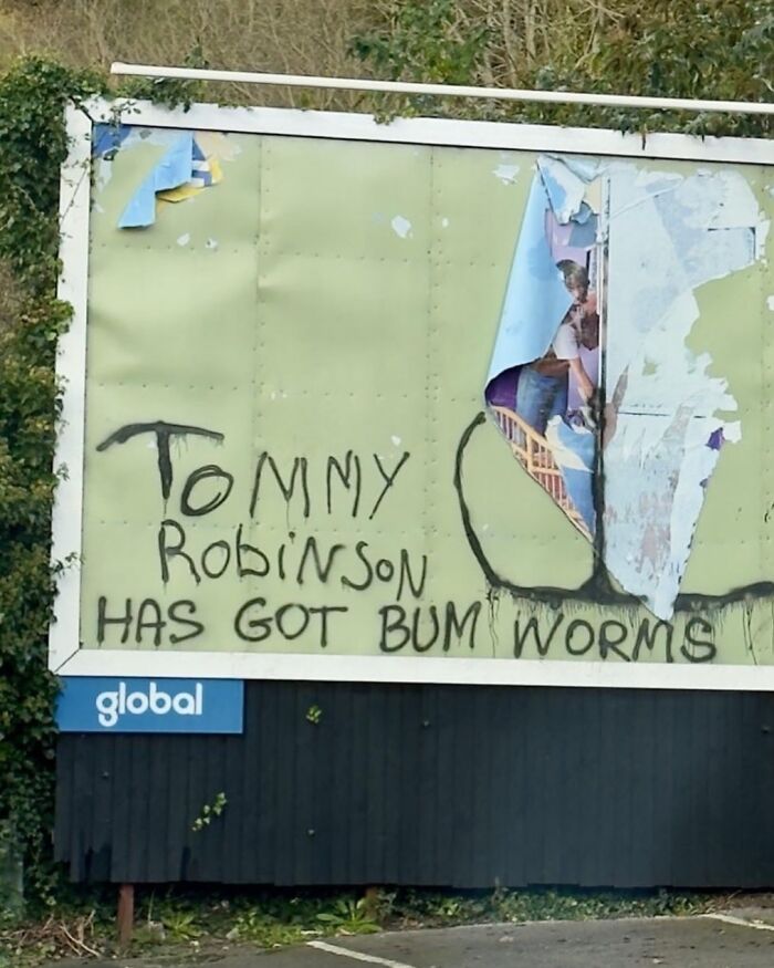 Graffiti on a billboard reads "Tommy Robinson has got bum worms," showcasing British humor.