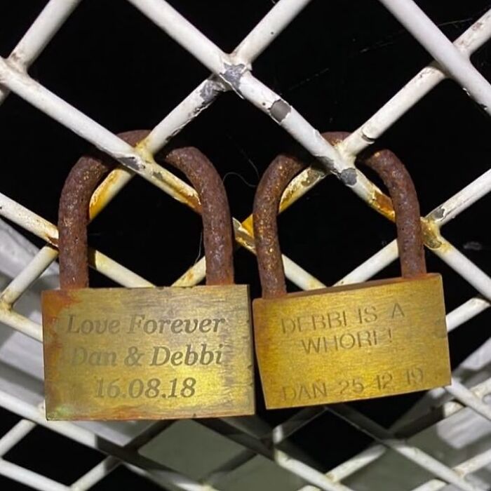 Two engraved padlocks on a metal fence displaying conflicting messages, possibly confusing to those unfamiliar with British humor.