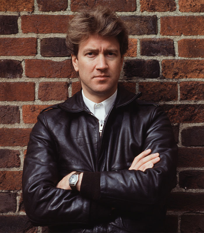 "Man in leather jacket standing against a brick wall, embodying David Lynch quotes on questioning reality."