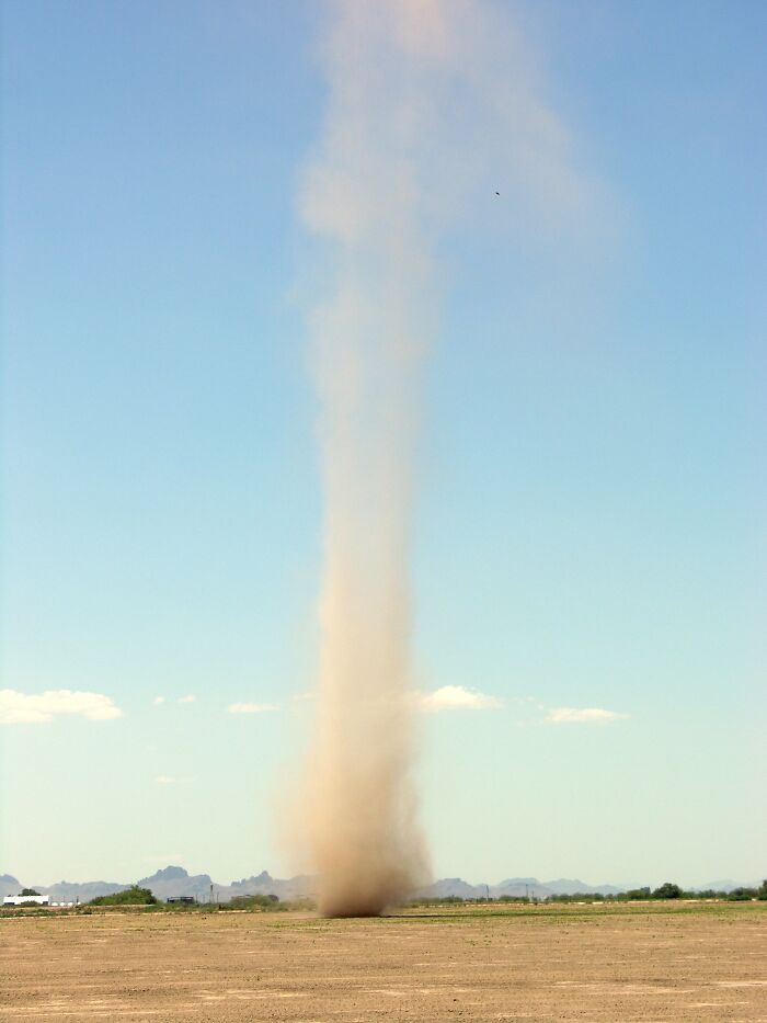 Dust devil spiraling upward in a wide, open landscape, showcasing strange natural phenomena.