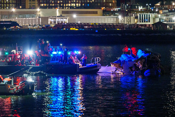 Rescue boats at night responding to DC plane crash, water illuminated by emergency lights.