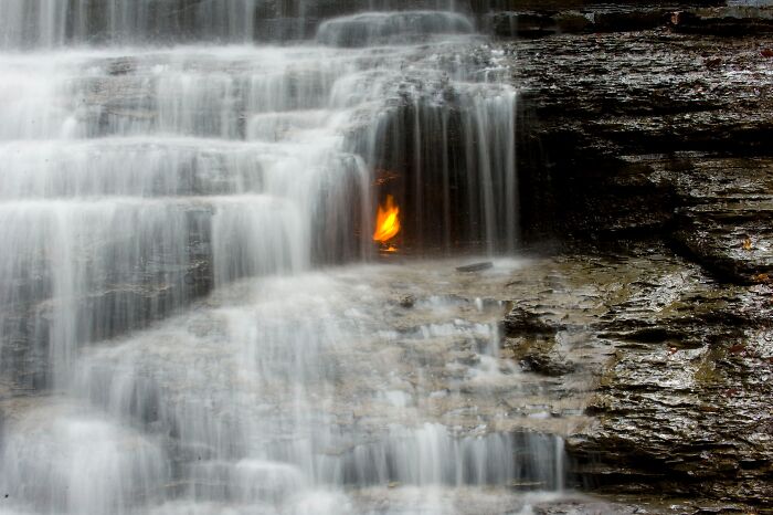 Waterfall with a natural flame burning behind it, showcasing incredible and strange natural phenomena.