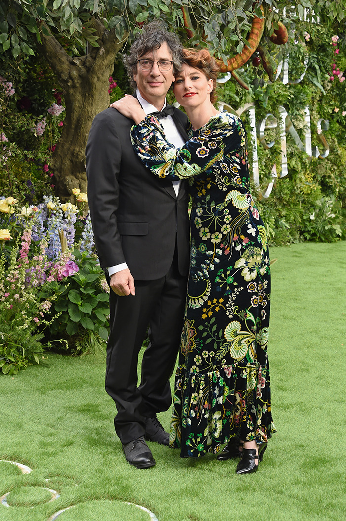 Neil Gaiman with ex-wife at an outdoor event, surrounded by lush greenery and colorful flowers.