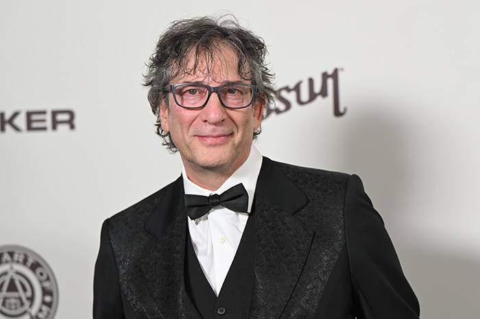 A person in a formal suit poses at an event, related to Neil Gaiman's ex-wife and recent allegations.