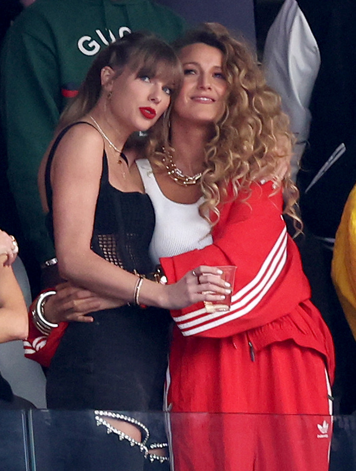 Two women embracing at an event, one in a black outfit and the other in a red tracksuit.