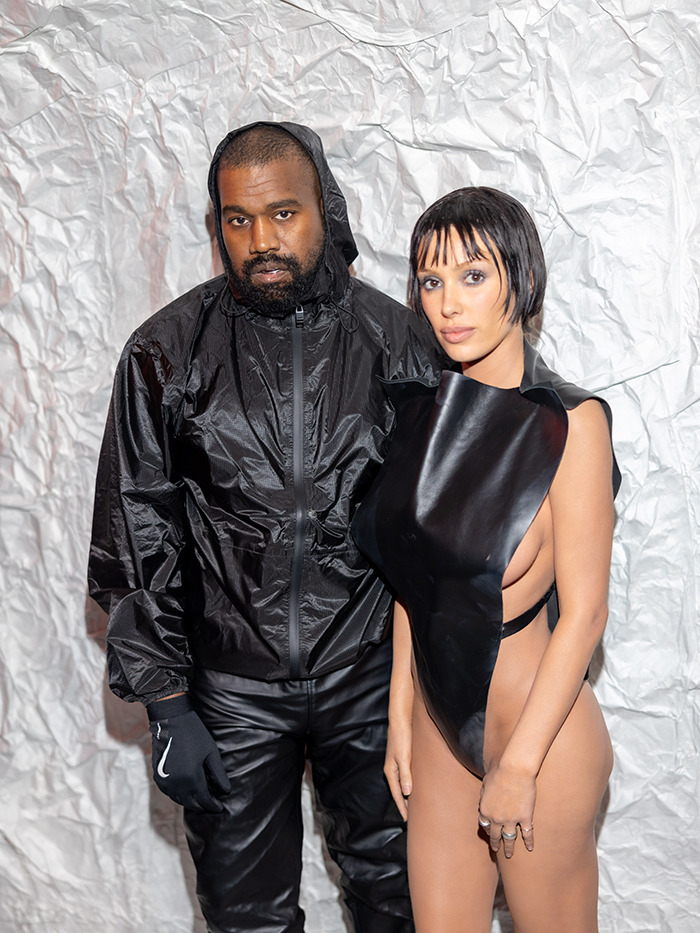 A couple poses in stylish black outfits against a textured backdrop.