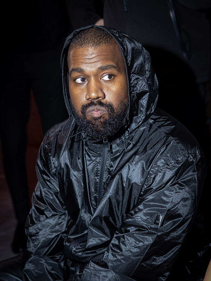 A man in a black jacket sits indoors, appearing thoughtful, under low lighting.