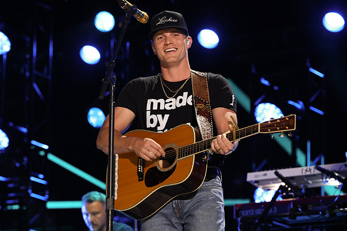 Musician playing guitar and singing on stage at inauguration event with bright lights in the background.