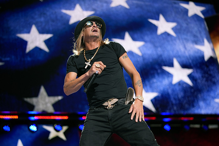 Singer performing at presidential inauguration, wearing a black outfit and hat, with an American flag backdrop.