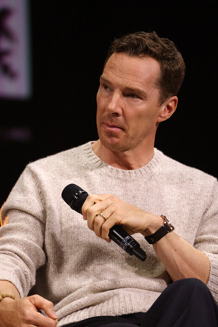 Benedict Cumberbatch speaking into a microphone wearing a beige sweater.