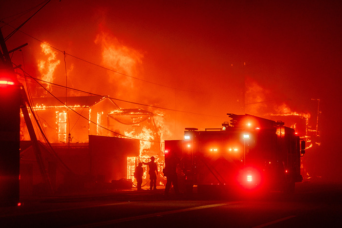 Firefighters and truck battling a blazing building, flames illuminating the scene at night.