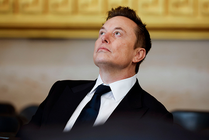 Elon Musk at presidential inauguration event, looking upwards, wearing a suit and tie.