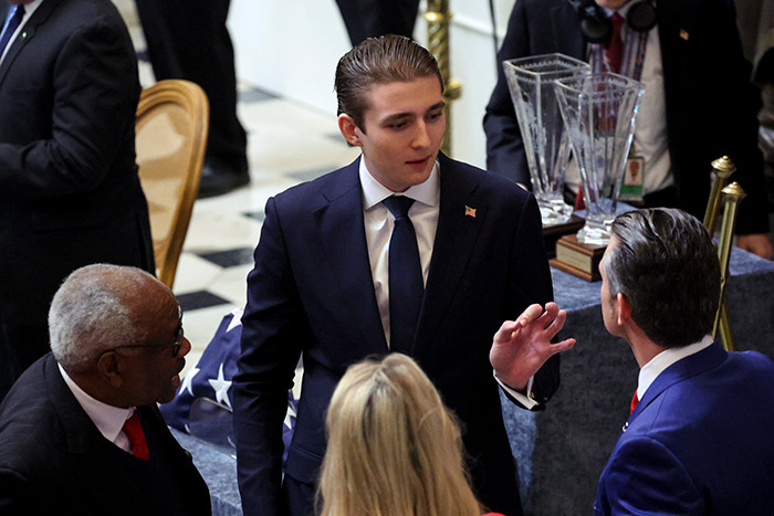 Barron Trump in a suit at the inaugurationt, surrounded by people.