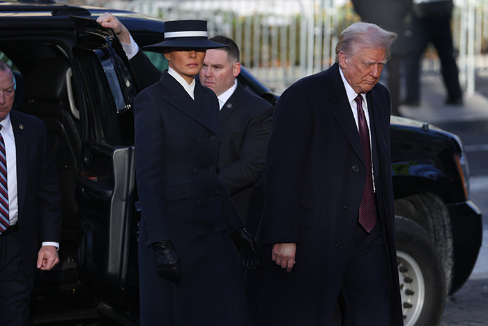 Melania Trump in a dark outfit and hat at a public event, accompanied by security, sparking humorous reactions.