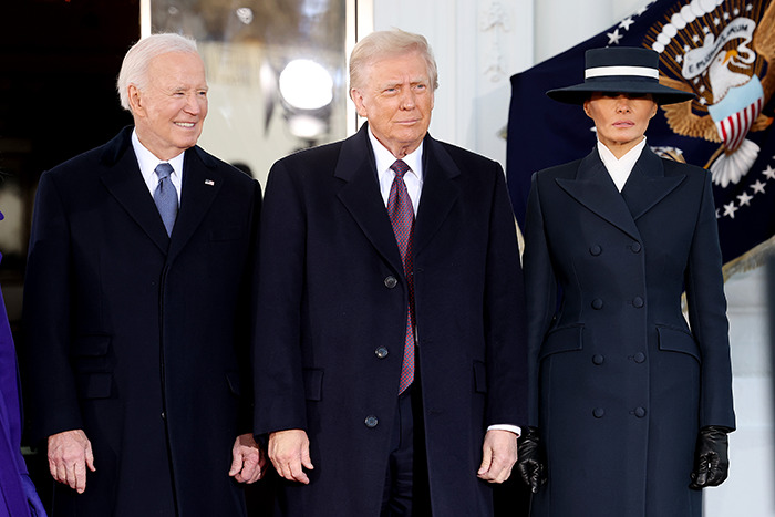 Melania Trump's outfit at the inauguration, wearing a dark coat and hat, standing with officials.