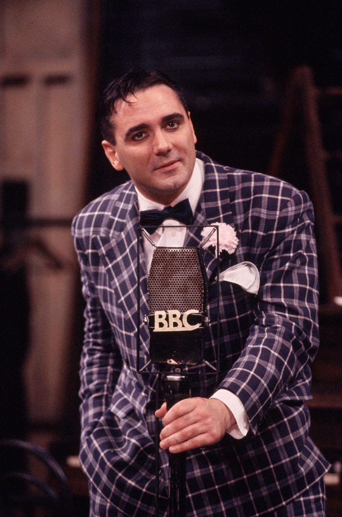 Man in plaid suit and bow tie with BBC microphone, related to 'Whose Line Is It Anyway?' star's legacy.