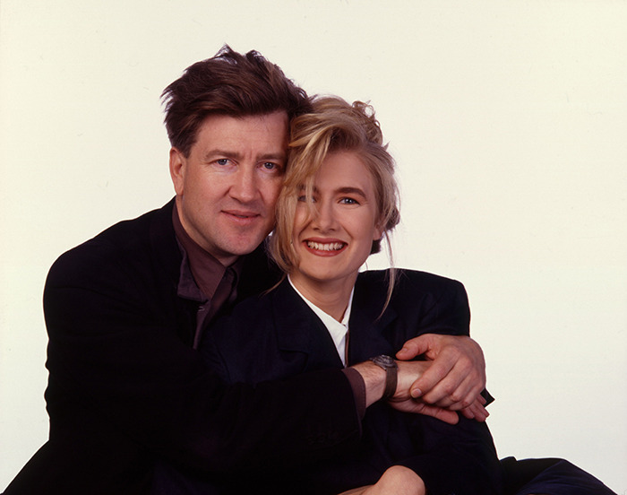 Laura Dern with David Lynch, both smiling, wearing dark jackets in a close embrace.