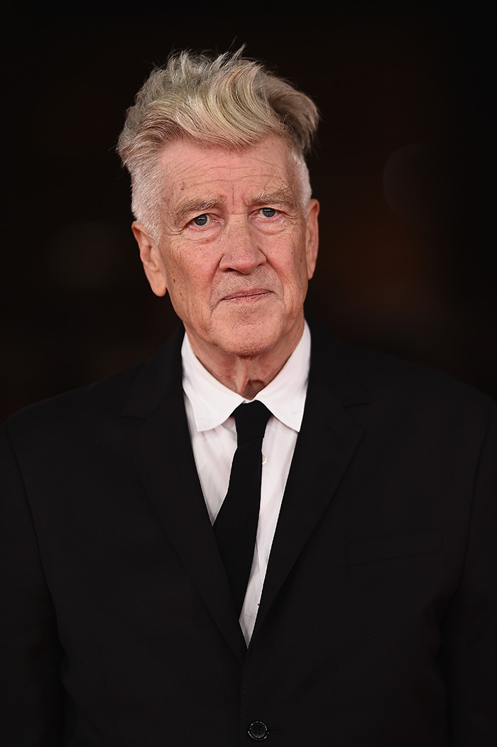 Man in a suit with distinctive hairstyle at a formal event, with Hollywood tributes pouring in for his work.