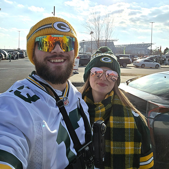 Packers fans in team gear tailgating outside a stadium.