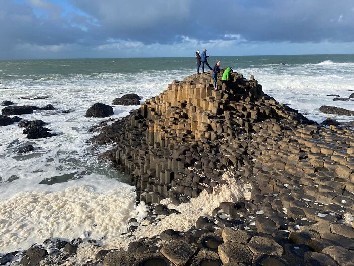 People standing on the Giant's Causeway, showcasing strange natural phenomena with hexagonal basalt columns by the sea.