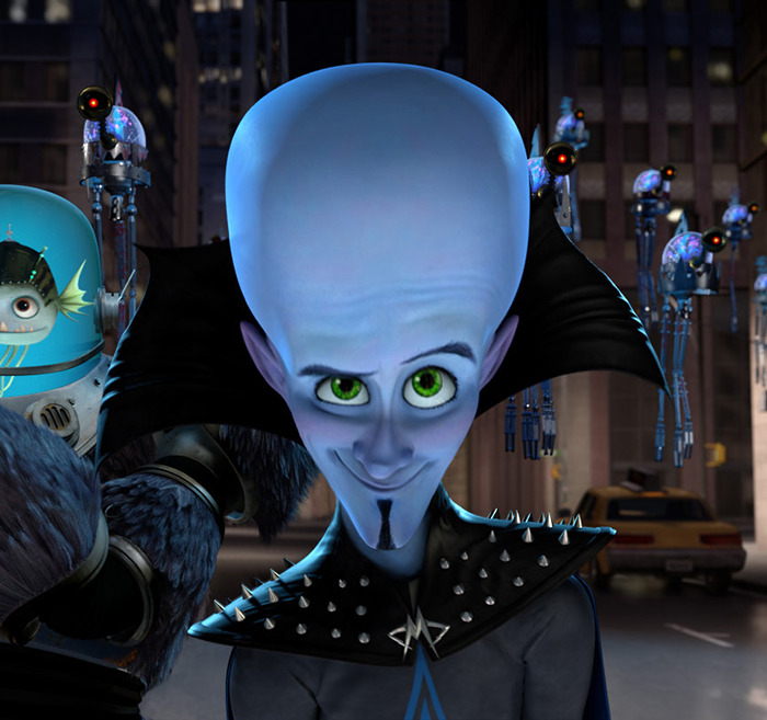 Character resembling 'Megamind' with a large blue head and green eyes, wearing a spiked black outfit in a cityscape.