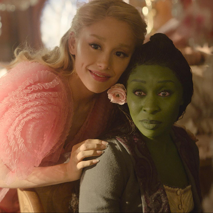 Cynthia Erivo and Ariana Grande costume, one with green makeup, embrace in a whimsical setting.