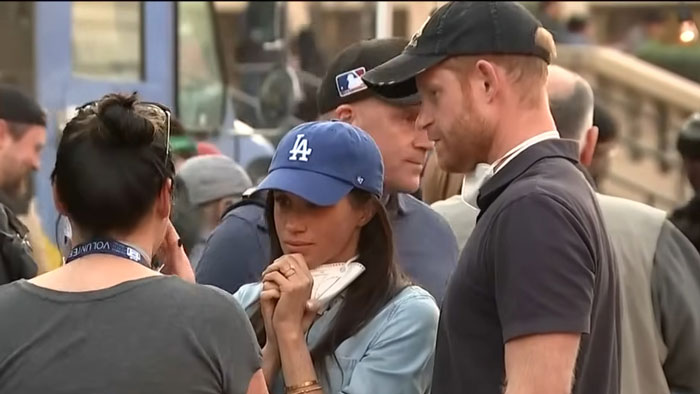 A group of people wearing casual clothes and hats in a crowded urban setting.