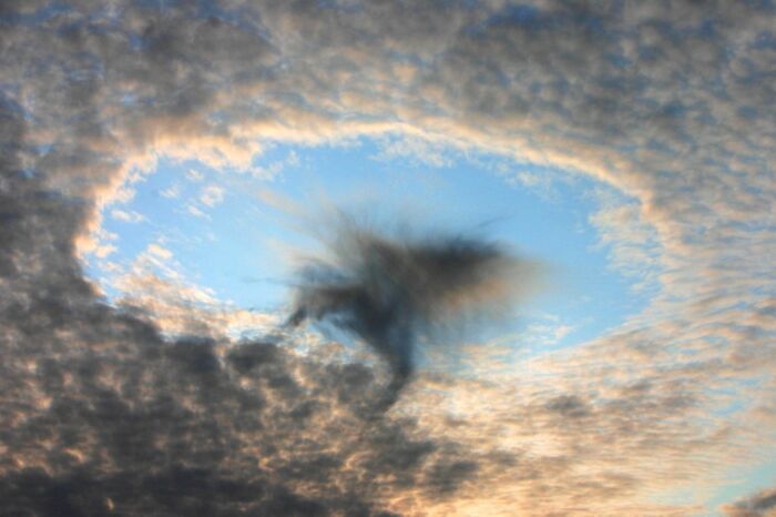 A stunning natural phenomenon with a fallstreak cloud creating a dramatic hole in the sky, surrounded by fluffy clouds.