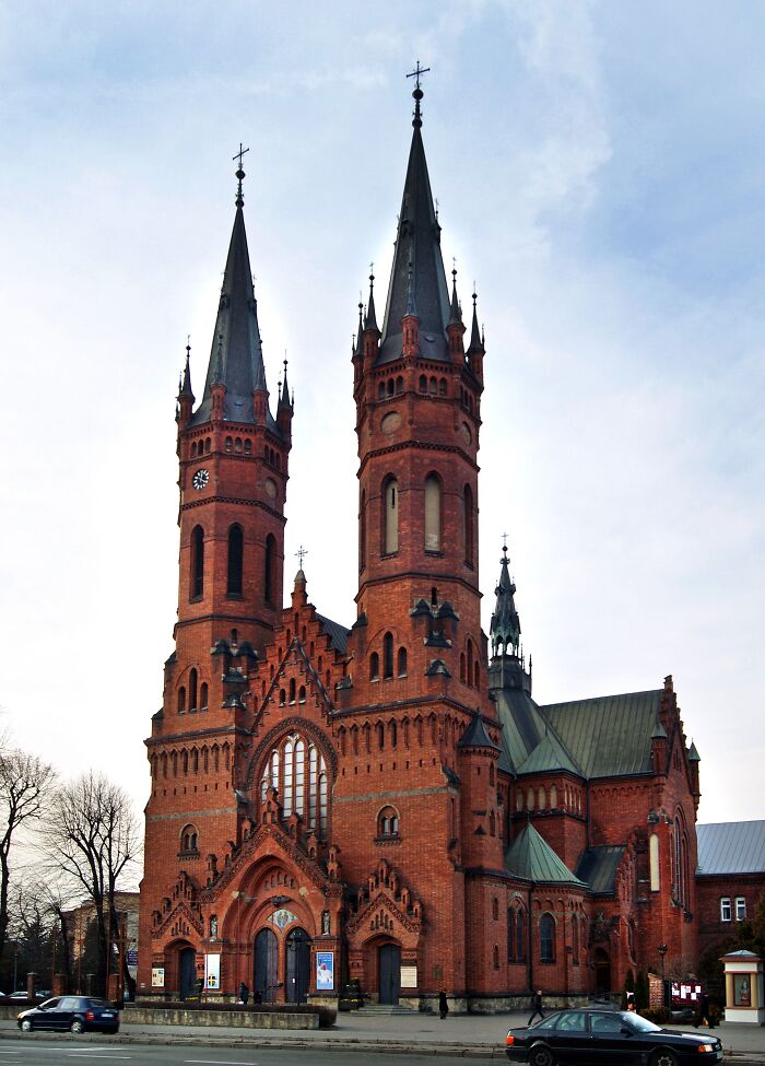 Majestic red brick church with twin spires under a clear sky, showcasing fascinating architecture details.