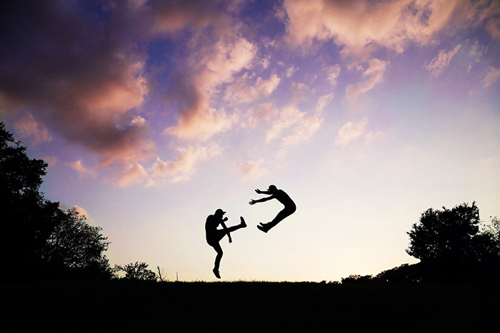 Silhouetted people jumping playfully against a colorful sky, capturing a funny-camera-roll moment.