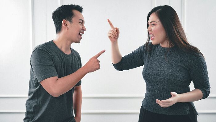 Couple in a heated discussion, both pointing fingers, indoors.