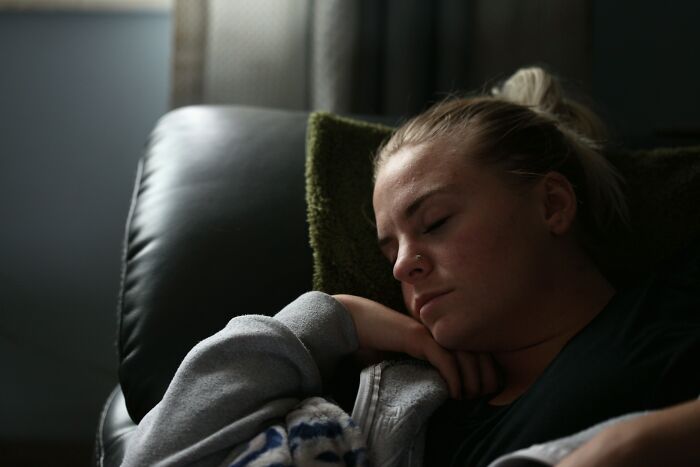 Woman resting on a sofa, appearing contemplative and relaxed, with soft lighting from a nearby window.