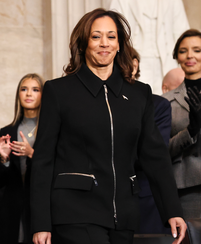 A woman in a black suit at a presidential inauguration event, surrounded by applauding attendees.