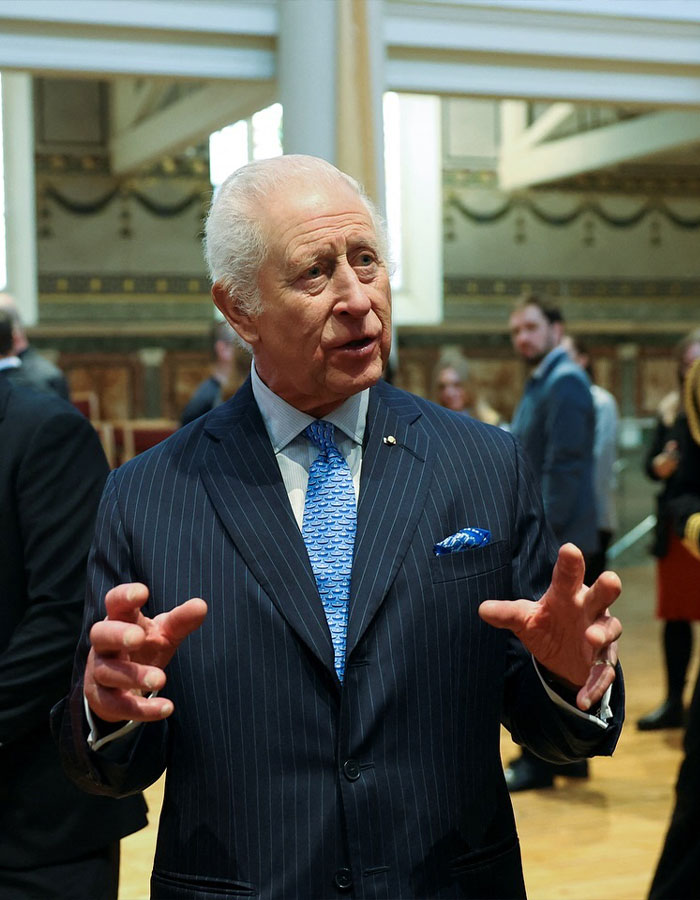 Man in a striped suit gestures while speaking, with people in the background, related to UK dentist shortage discussion.