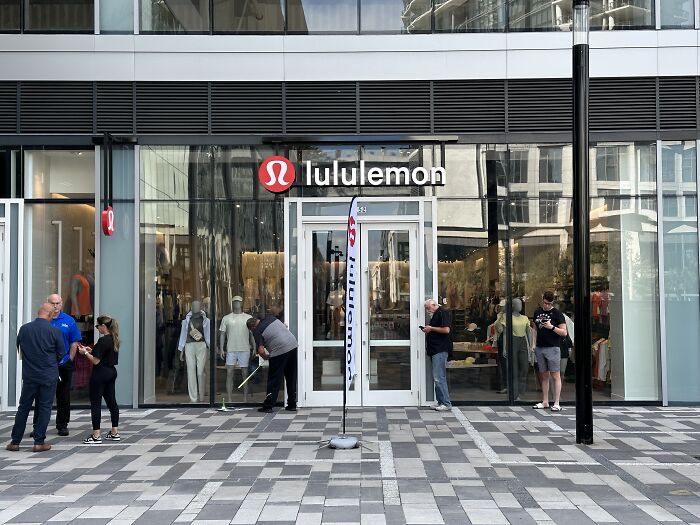 Lululemon storefront with several people outside, featuring modern architecture and glass facade.