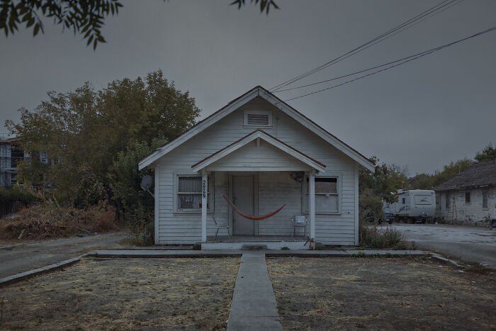 Suburban house with a porch and hammock, capturing disconnection through muted colors and empty surroundings.