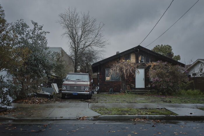 Suburban disconnection depicted by an old van parked outside a weathered house on a gloomy day.