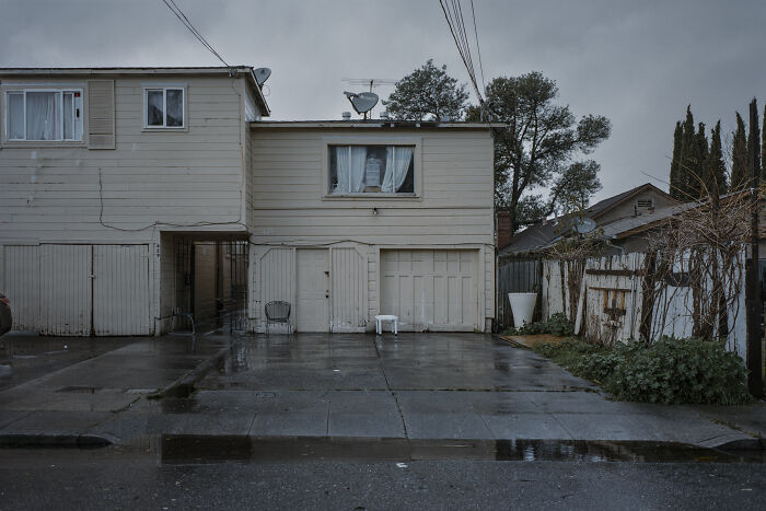 Suburban disconnection depicted in a quiet, rainy neighborhood scene by Mischa Lluch.