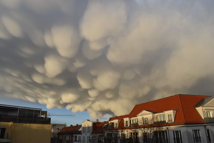 Mammatus clouds, a stunning natural phenomenon, looming over buildings with red rooftops at sunset.