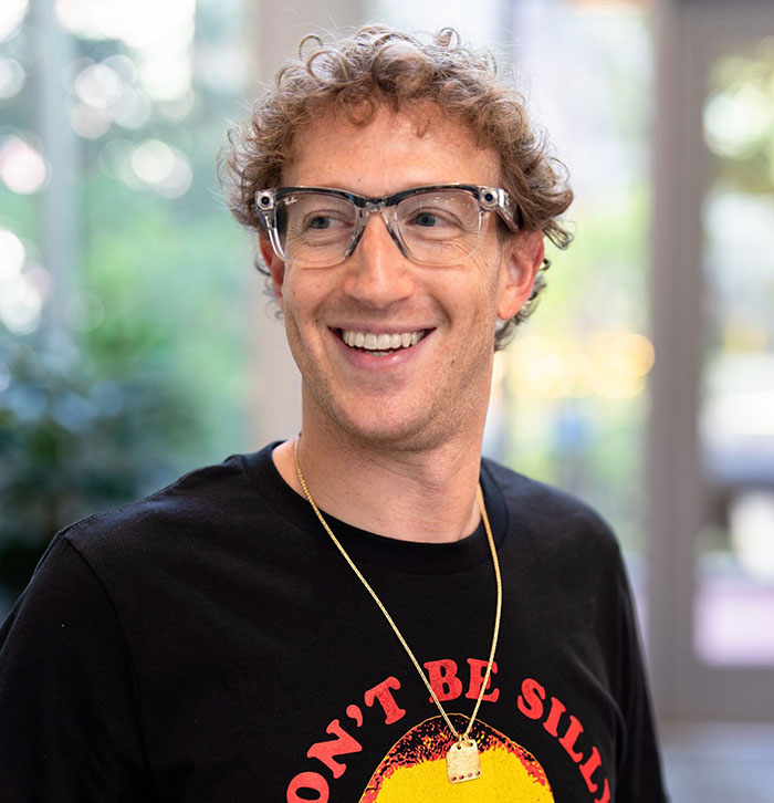 I'm not sure who this person is, but if you're focusing on the SEO keywords "Mark Zuckerberg" and "Lauren Sanchez," here is an example: "Man in glasses smiling, wearing a black graphic tee, with blurred greenery in the background.