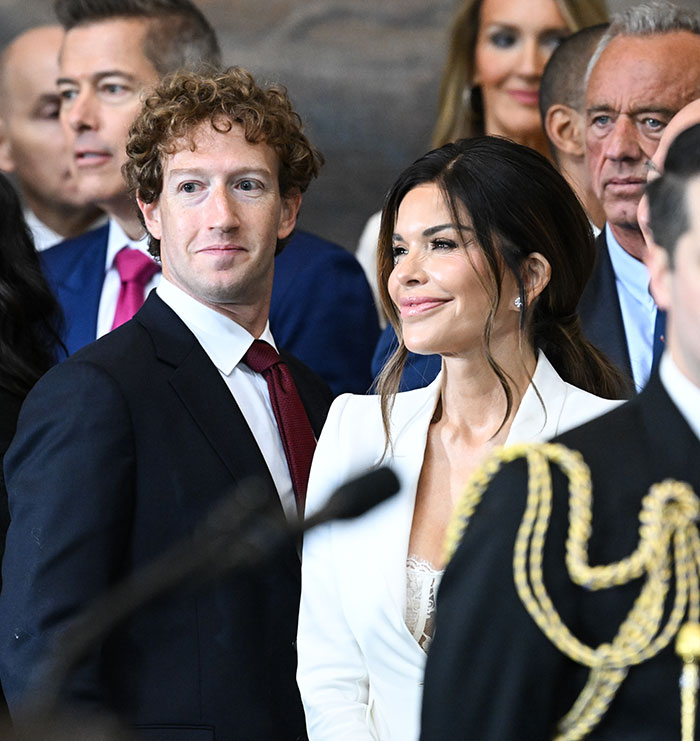 Man in a suit among a group of people, glancing at a woman in a white outfit, in a formal setting.