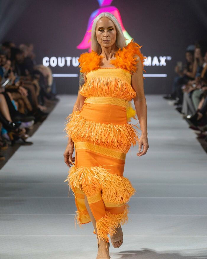 Fashion prodigy dress design showcased on a runway, featuring vibrant orange and feather details.