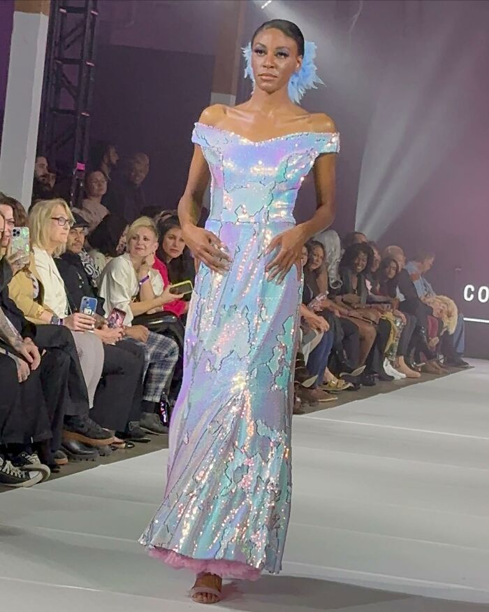 Model wearing a shimmering dress designed by an 8-year-old fashion prodigy during a runway show.