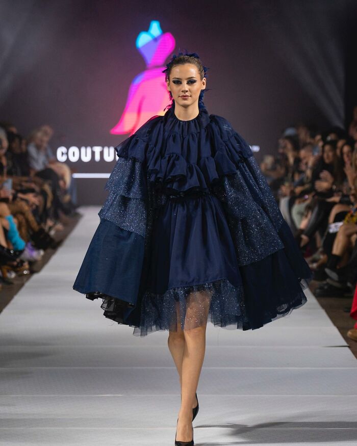 Model in a blue dress walking a runway at a fashion show designed by an 8-year-old prodigy.