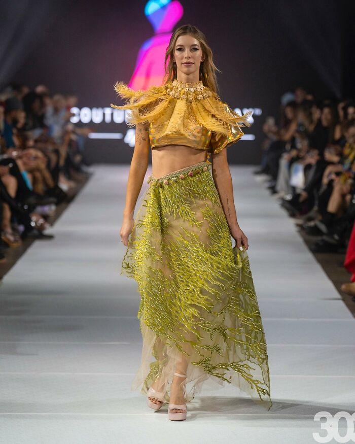 Model wearing a yellow and gold dress on a runway designed by a young fashion prodigy.