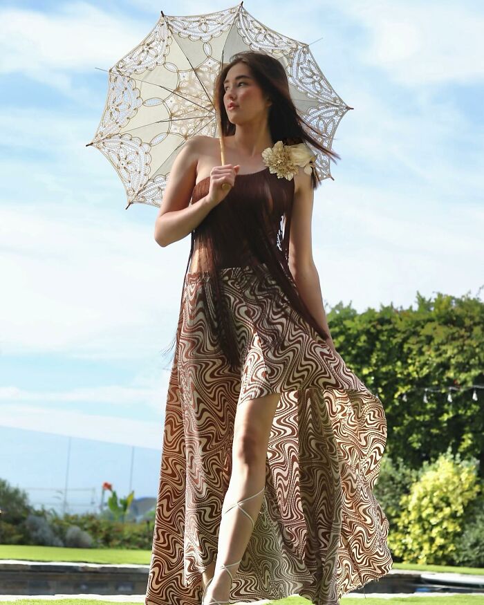 Fashion prodigy in a patterned dress with lace umbrella, standing outdoors in daylight.